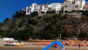 A boat docked near a beach with a backdrop of white buildings and a rocky hillside. - Casa Vacanza Nibbio 26 (Sperlonga)
