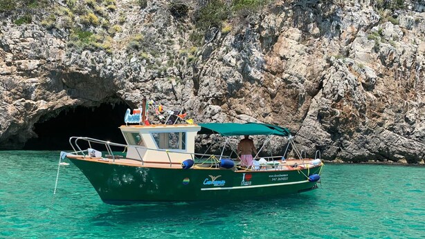 A boat with a cabin, a person standing at the front, and a rocky cliff in the background. - Casa Vacanza Nibbio 26 (Sperlonga)