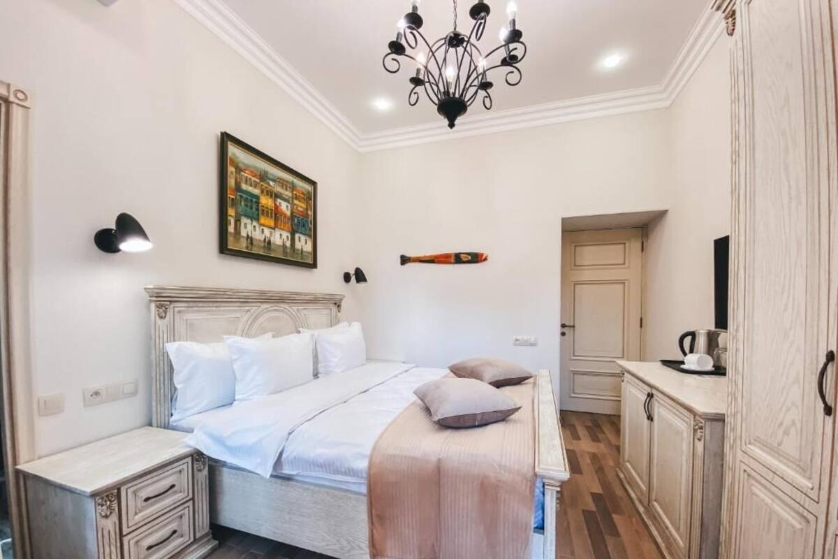 Un dormitorio con cama, mesitas de noche, una araña, un cuadro y un armario.