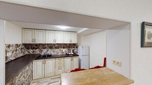 Una cocina compacta con armarios blancos, salpicadero de azulejos y un refrigerador.