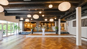 A spacious lobby with a wooden herringbone floor, large windows, and hanging spherical light fixtures.