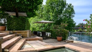 A patio with a pool, stone steps, outdoor furniture, and a view of a bridge.
