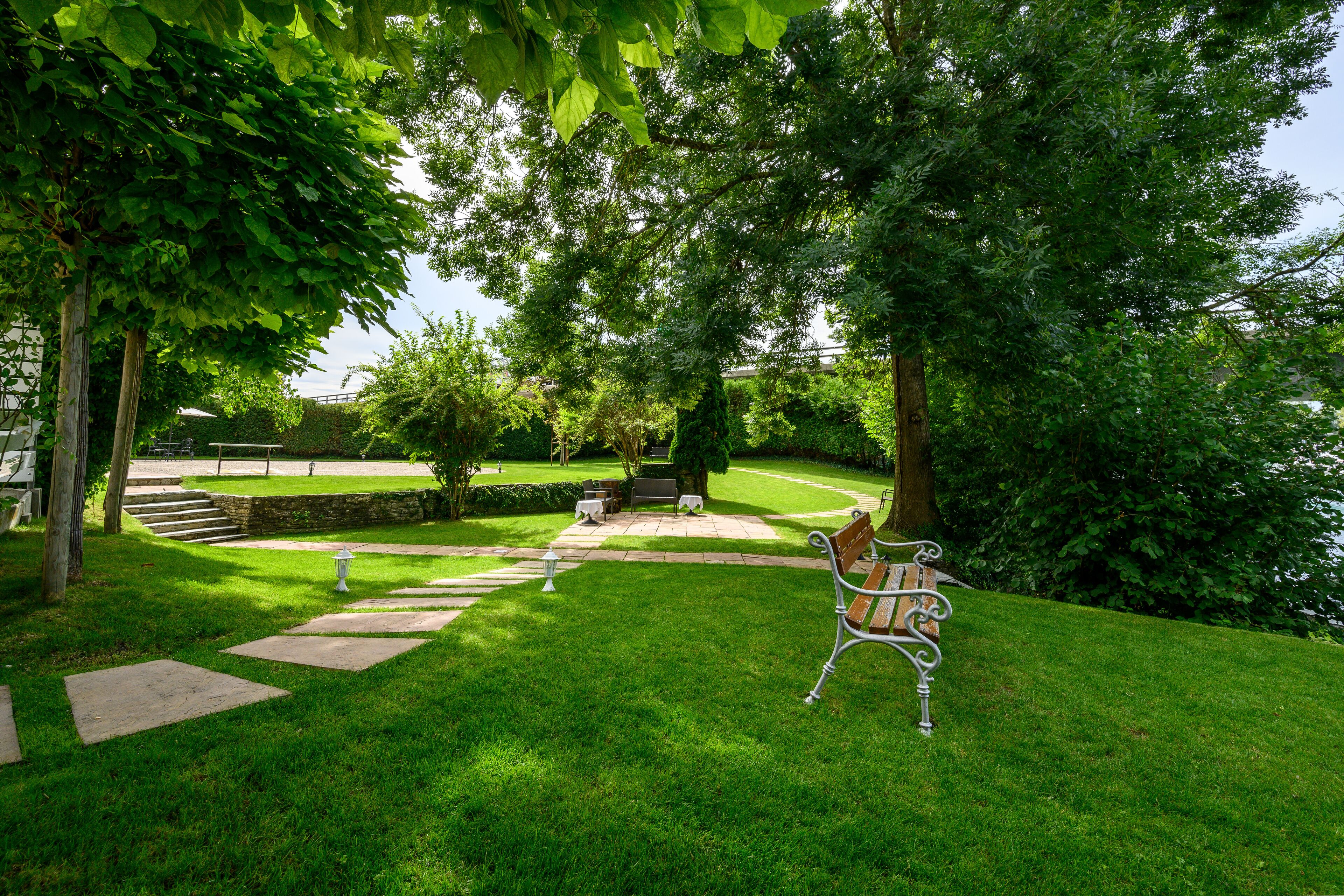 Ein gepflegter Garten mit einem gepflasterten Weg, einer Bank und einem Tisch, gedeckt für ein Essen im Freien.