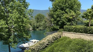 A view of a river with boats, surrounded by trees and a stone wall.