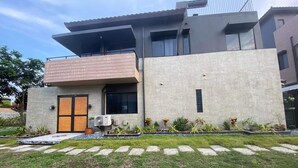 Una casa moderna de dos pisos con techo plano, ventanas grandes y un balcón.