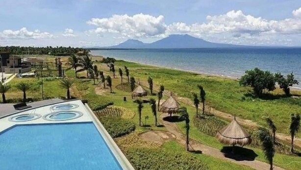Un resort con piscina, playa y una montaña al fondo.