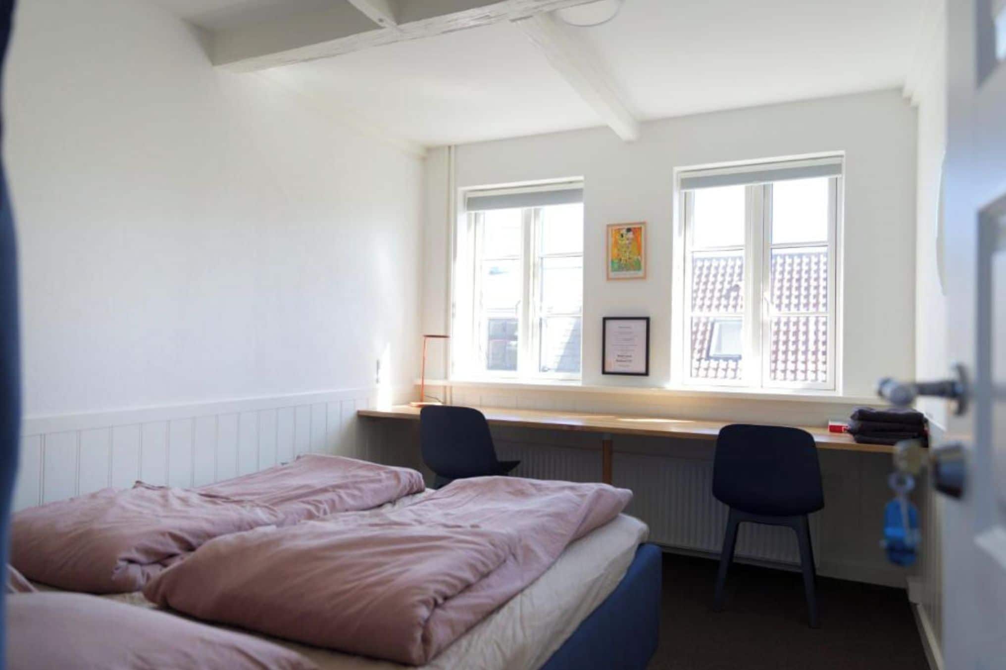 Un dormitorio con una cama, dos sillas, un escritorio y una ventana con persianas.