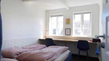 Un dormitorio con una cama, dos sillas, un escritorio y una ventana con persianas.