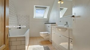 Un baño con bañera, inodoro y tocador con espejo.