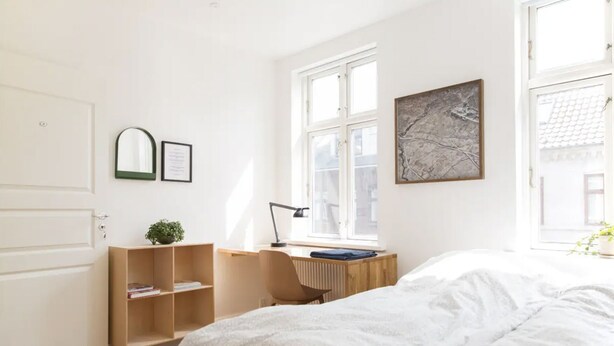 Un dormitorio con cama, un escritorio con silla, un radiador, una ventana y una puerta.