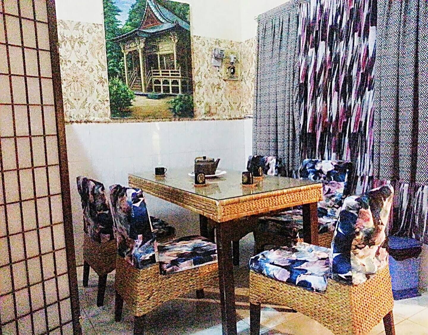 Ein Essbereich mit einem Holztisch und Korbstühlen, einem Bild eines traditionellen Gebäudes an der Wand und einem gemusterten Vorhang.