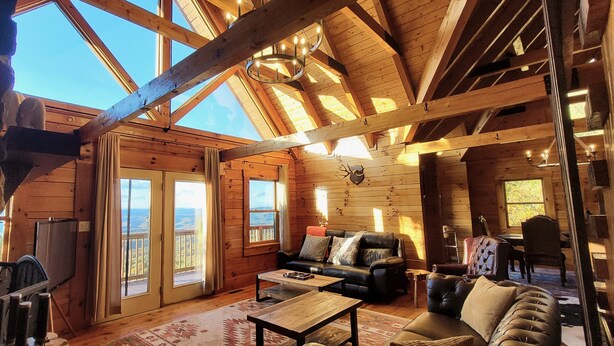 A cozy cabin interior with a wooden interior, a fireplace, a sofa, and a dining area.