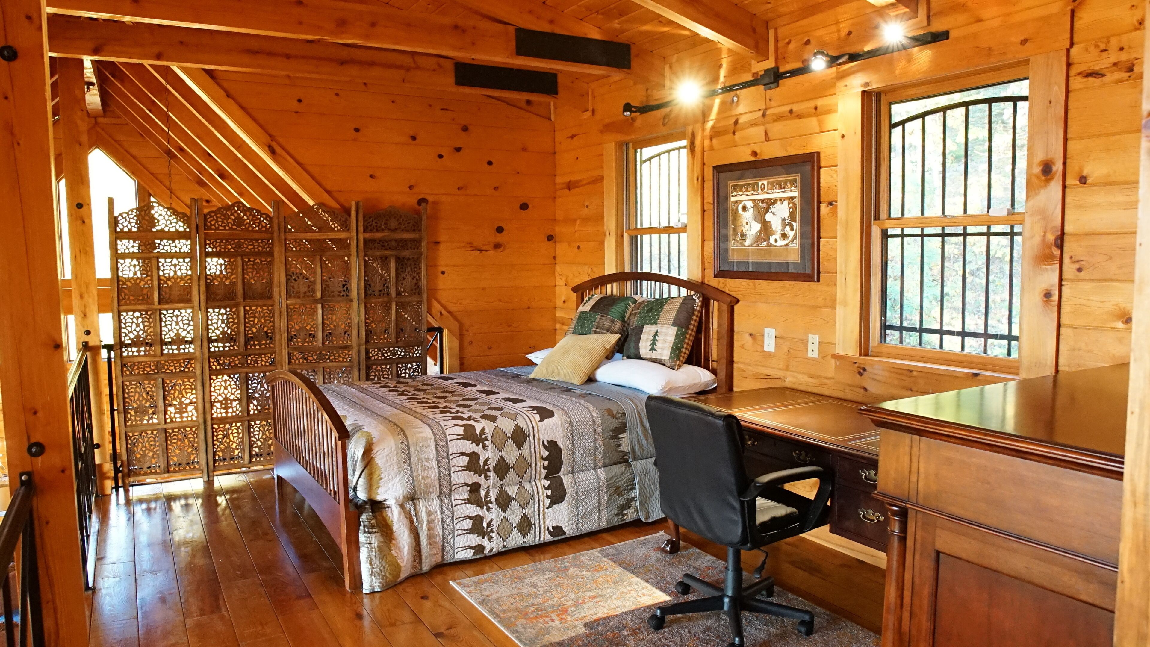 A wooden cabin bedroom with a bed, desk, and chair.