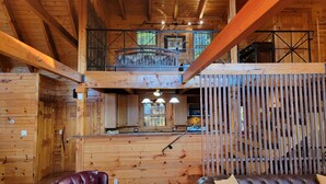 A wooden cabin interior with a dining area, kitchen, and a balcony with a metal railing.