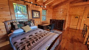 A wooden cabin bedroom with a bed, desk, and dresser.