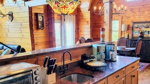A rustic cabin interior with a wooden interior, a kitchen with a large island, a coffee maker, and a clock on the wall.