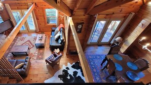 A spacious loft-style room with a stone fireplace, leather sofas, a dining table, and a cowhide rug.