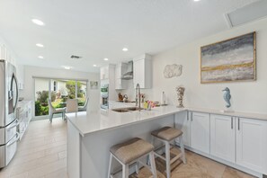 Cozinha moderna com armários brancos, uma ilha grande com banquetas, vista para o exterior e um enfeite de cavalo-marinho na parede.