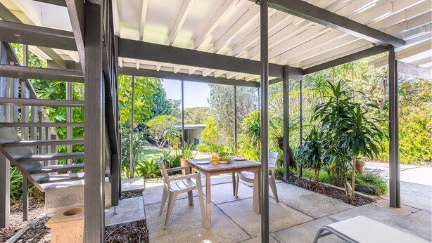 A covered outdoor patio with a table and chairs, surrounded by lush greenery. - 23 Lentara St - pet friendly, air con, Wi-Fi, boat parking (Fingal Bay)
