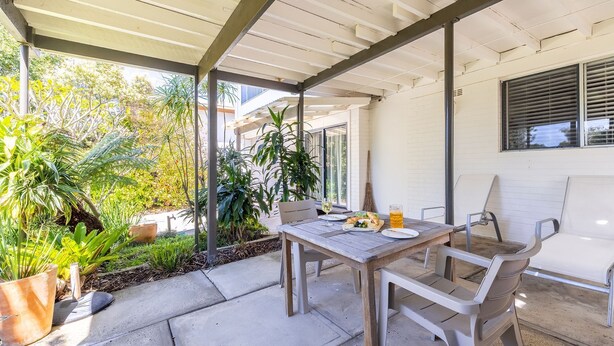 An outdoor patio with a table set for two, surrounded by potted plants and a white wall. - 23 Lentara St - pet friendly, air con, Wi-Fi, boat parking (Fingal Bay)