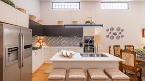 Une cuisine moderne dotée d’un îlot central, d’appareils électroménagers en acier inoxydable et d’un coin repas avec des chaises en bois et un vase de fleurs.