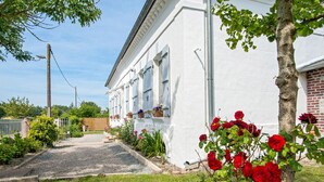 A white building with a gravel driveway, a tree with red flowers, and a brick wall. - Villa du Ridin - La Villa 4 Fleurs (Le Crotoy)