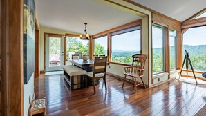 A spacious room with wooden flooring, large windows offering a mountain view, a dining area with a bench, and a tripod-mounted camera. - Mountain View/Jacuzzi/ Fire pit/ Close to Downtown. Pet Friendly!  (Murphy)