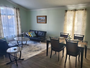 Un salon avec un canapé, une table basse et des fauteuils. Il y a un tableau au mur et une fenêtre avec des rideaux.