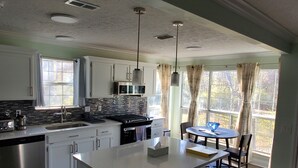A modern kitchen with white cabinets, a stainless steel dishwasher, a large island, and a dining area with a table and chairs.