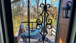 A hammock on a wooden deck with railings, a bench with cushions, and a lantern post.