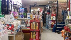Un petit magasin encombré, avec divers articles exposés sur des étagères et des cartons éparpillés sur le sol.