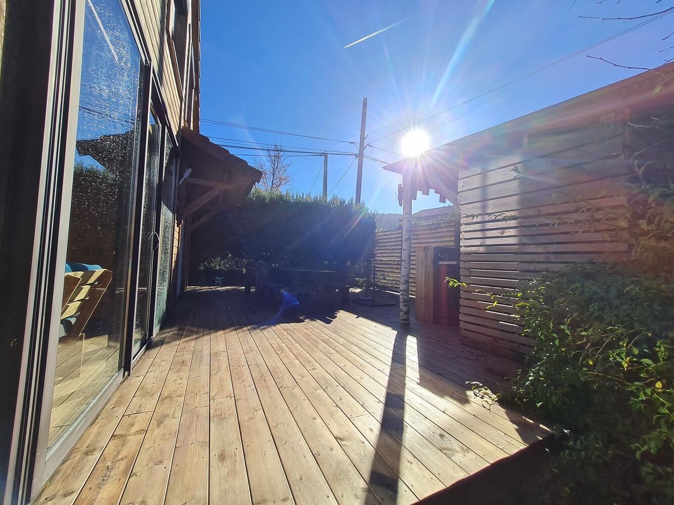Una terraza de madera con un ventanal de vidrio que da a una habitación.