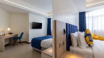 Ett hotellrum med en säng, ett skrivbord, en stol, en tv och ett fönster med gardiner.