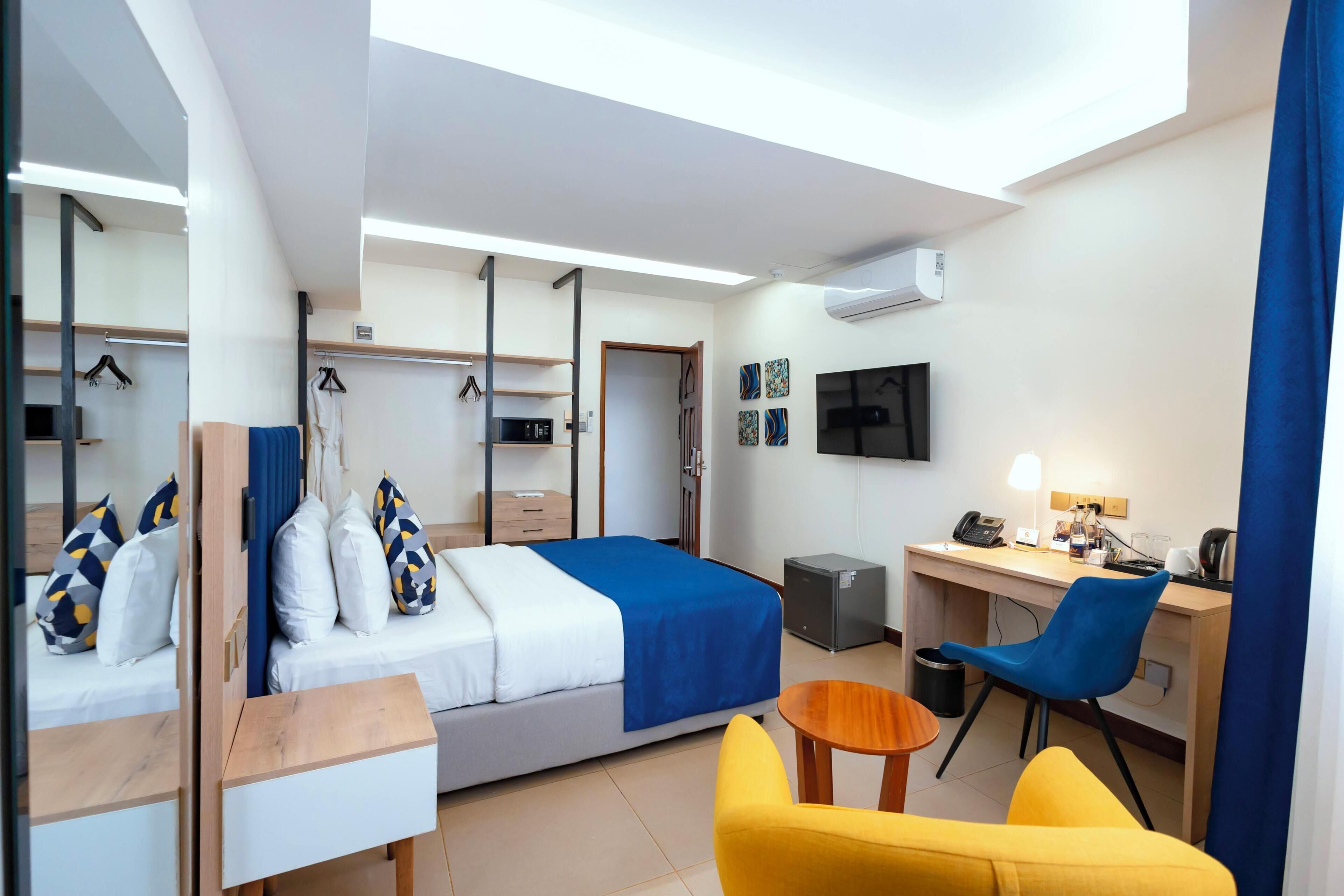A hotel room with a bed, a desk, a chair, a TV, and an air conditioning unit.