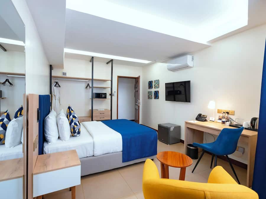 A hotel room with a bed, a desk, a chair, a TV, and an air conditioning unit.