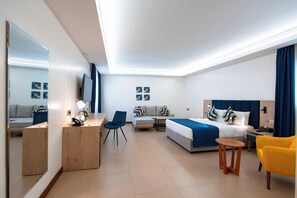 A modern hotel room with a bed, desk, chair, and a sofa.