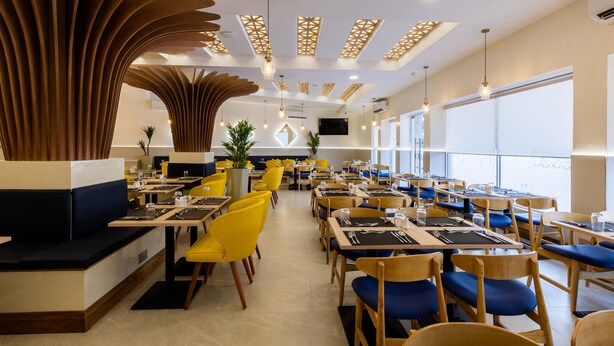 En moderne restaurant med gul og blå siddeplads, træindretning og store vinduer.