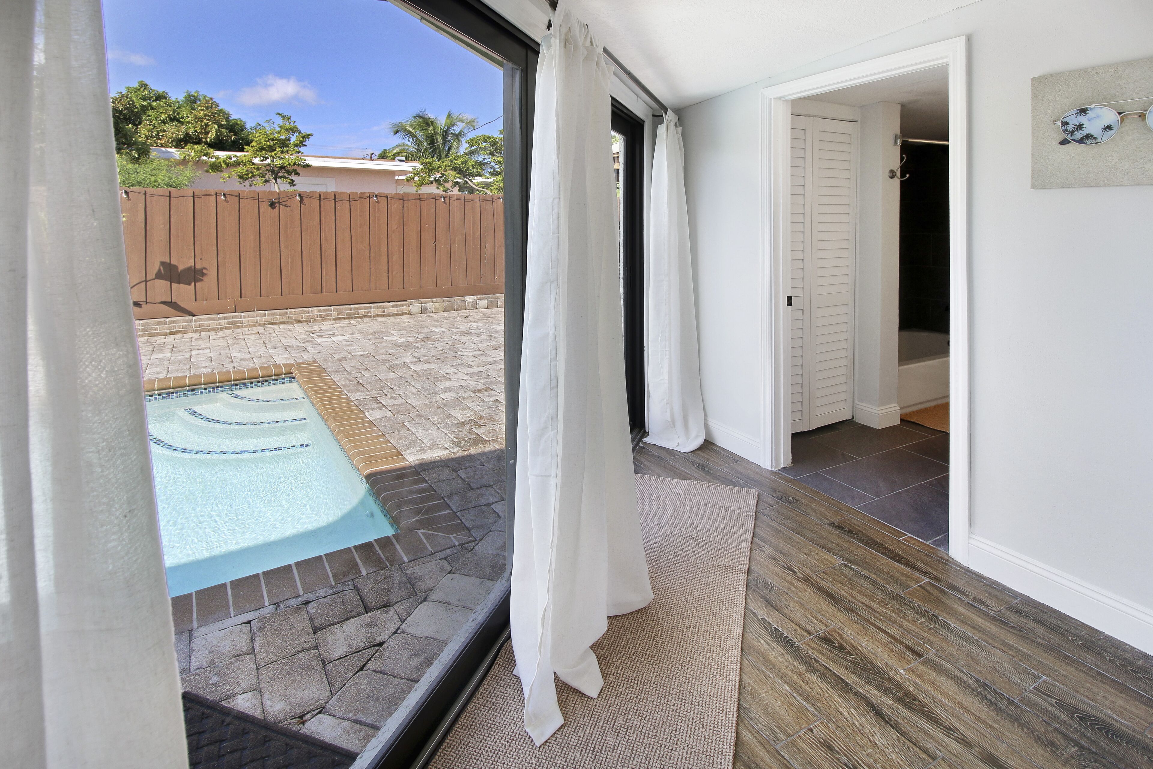 Blick von einem Balkon auf einen Garten mit Schwimmbad, einer Holzterrasse und einer Tür zu einem Badezimmer.