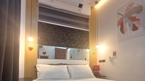 A hotel room with a large bed, a wall-mounted air conditioner, a mirror, and a small table with a lamp. - The Most Romantic Staycation in the City (Tacloban City)