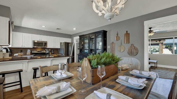 A modern kitchen with white cabinets, a wooden dining table set for four, and a chandelier. - Weitz Haven: Pool, Hot-tub, More! (Fredericksburg)