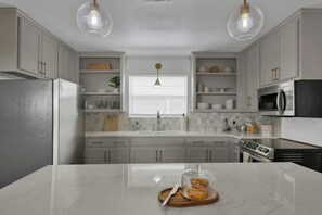 A modern kitchen with white cabinetry, a central island, stainless steel appliances, and pendant lighting. - Weitz Getaway with Private Pool + Two Hot Tubs (Fredericksburg)