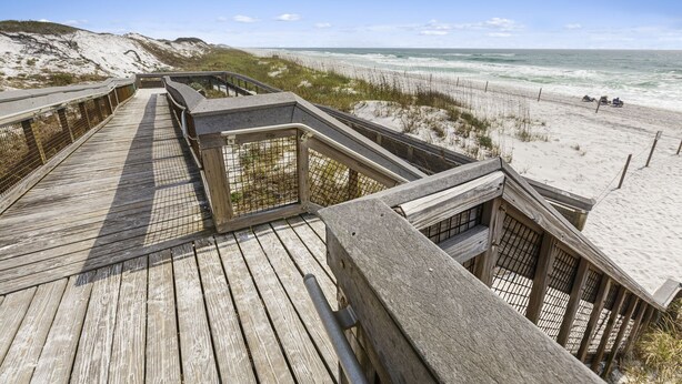 Une promenade en bois qui mène à une plage de sable et offre une vue sur l’océan.