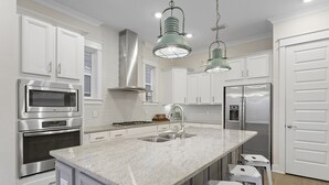 Une cuisine moderne avec des meubles blancs, des appareils en acier inoxydable, un plan de travail en granit et des luminaires suspendus.