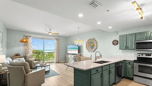 A modern kitchen with green cabinets, a large island, and a dining area with a view. - Beach Resort 402 - Gulf View, Zero-Entry Lagoon Pool, Hot Tub, Deeded Beach! (Miramar Beach)