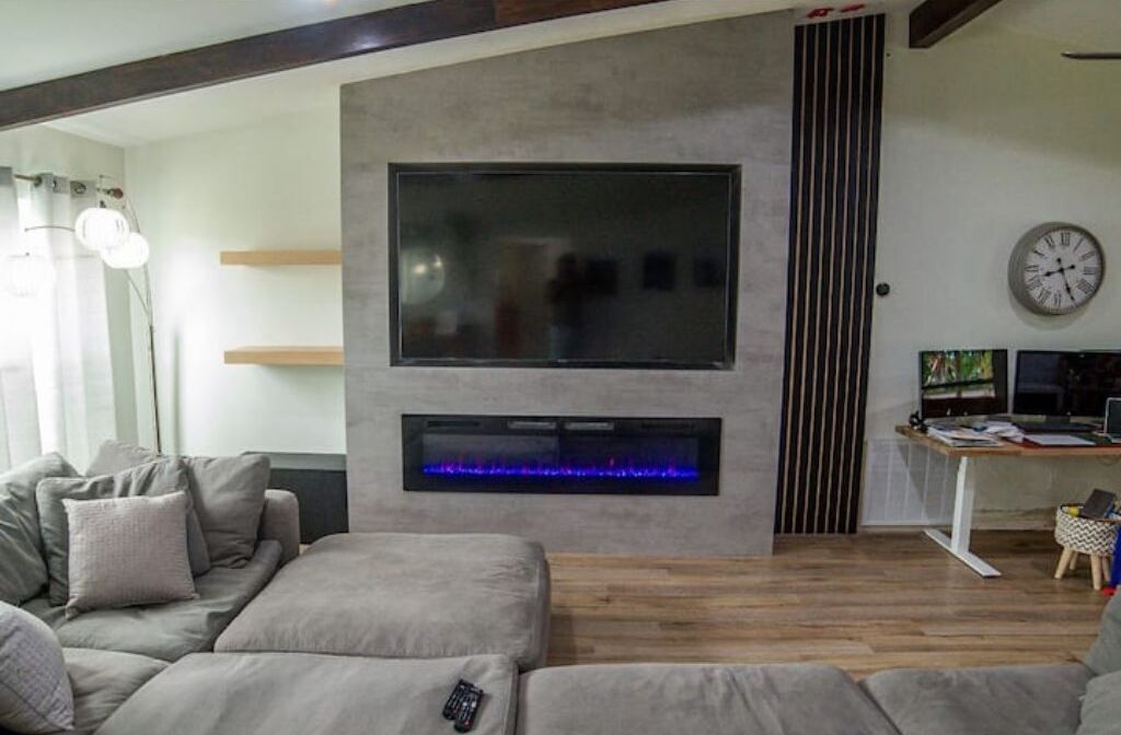 Un salon moderne avec un grand téléviseur à écran plat fixé au mur, une cheminée intégrée en dessous, une table basse en bois et un canapé gris.