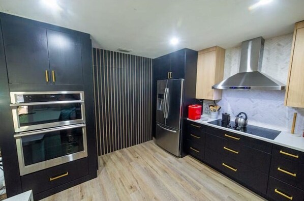 Une cuisine moderne avec des meubles de couleur noire, des appareils en acier inoxydable et un plancher en bois.