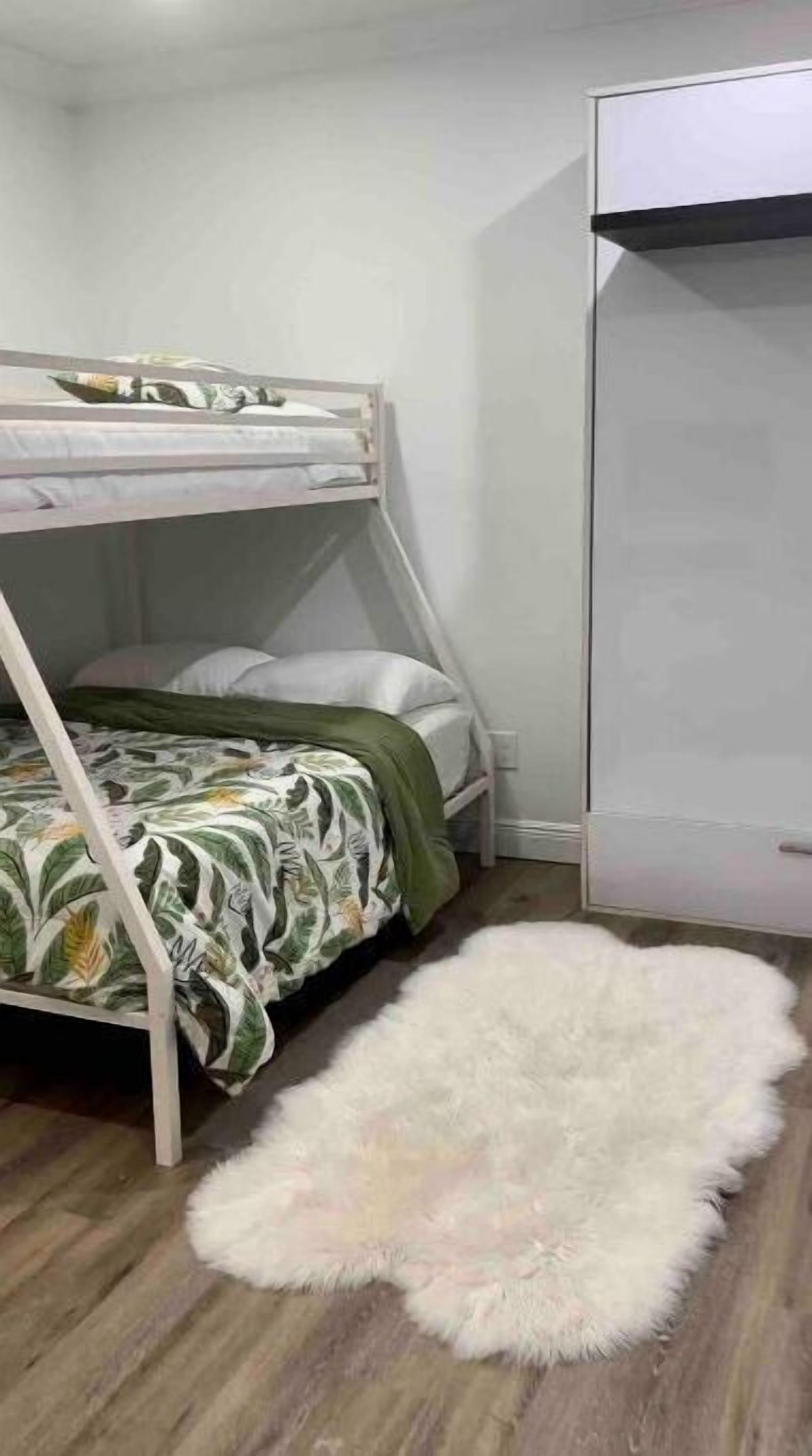 Ein Stockbett mit floralem Bettbezug, ein flauschiger weißer Teppich auf dem Boden und ein weißer Kleiderschrank in einem Schlafzimmer.