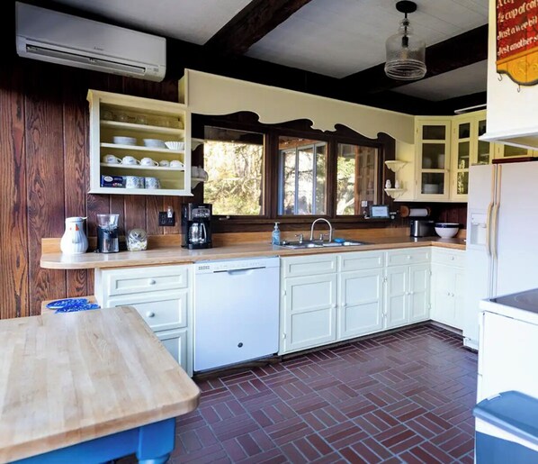 A kitchen with white cabinets, a wooden countertop, and a brick floor.