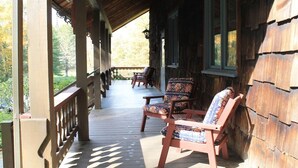 Eine hölzerne Veranda mit zwei Stühlen und einem Tisch, mit Blick auf einen Garten.
