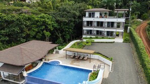 Un moderno edificio de dos pisos con piscina, rodeado de exuberante vegetación.